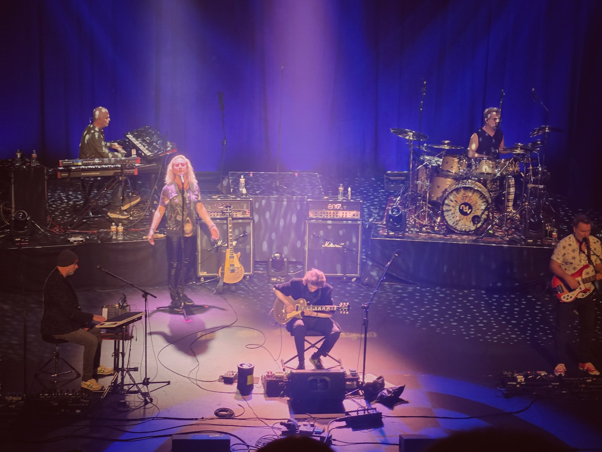A band on stage under blue light with Marshall amps and a drum kit