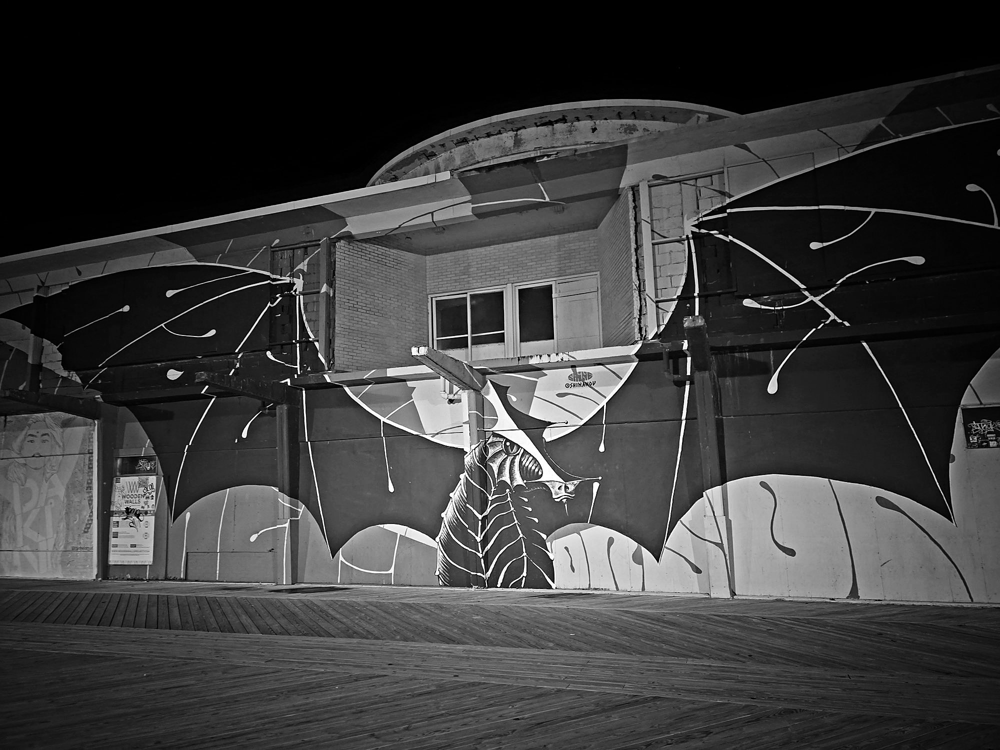 A large mural of a ray with outstretched wings on a building beside an empty boardwalk at night