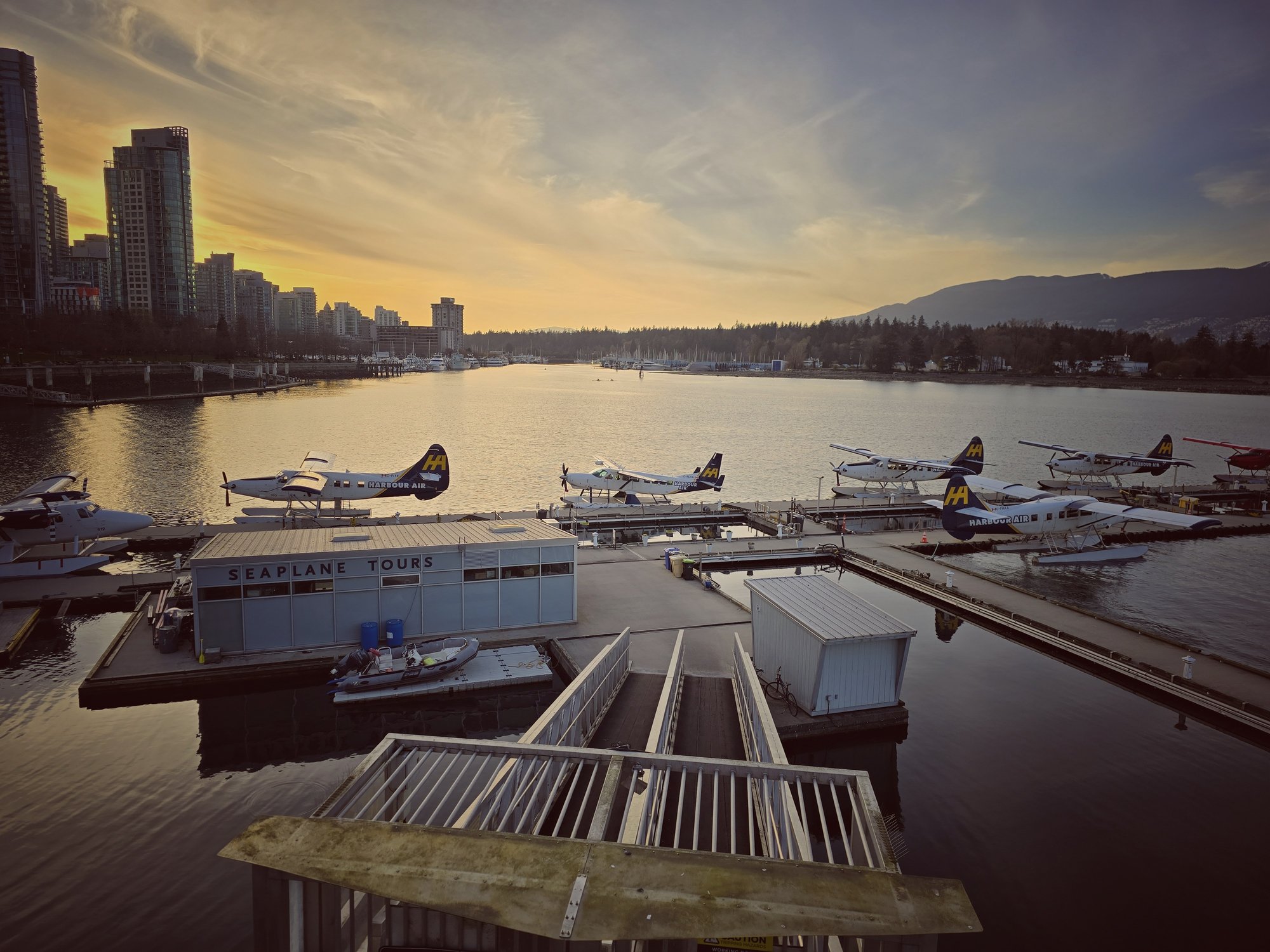 Floatplanes moored at the Coal Harbour seaplane dock at sunset with the Vancouver skyline