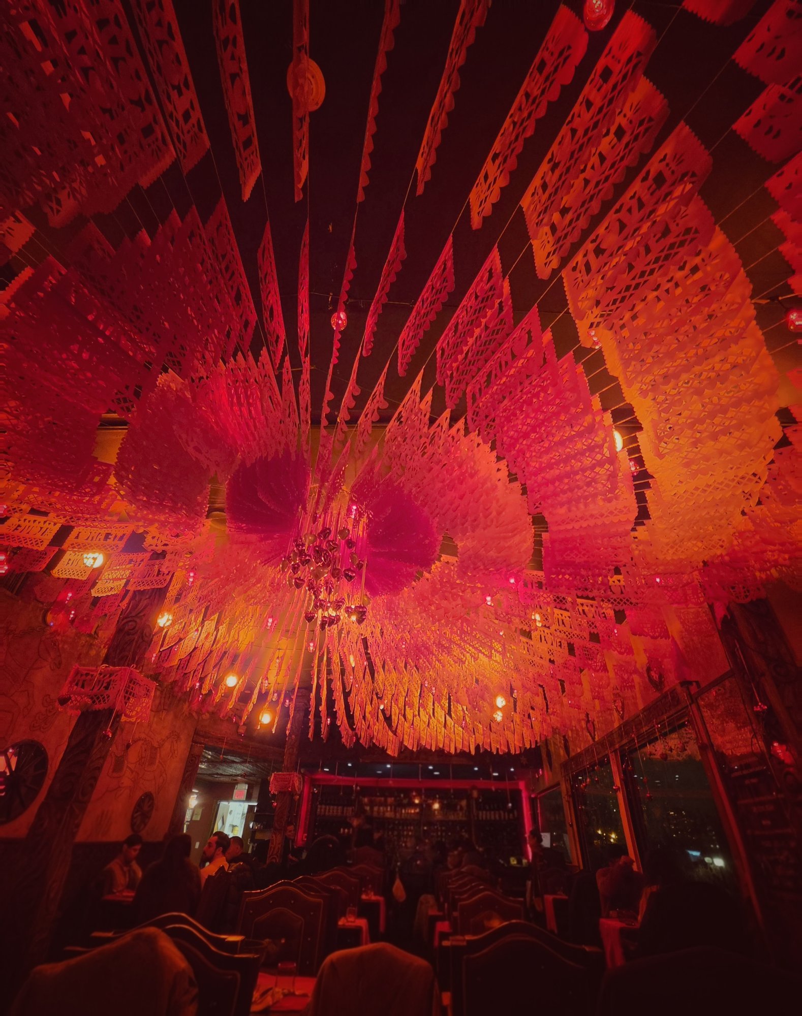 A restaurant ceiling covered in red and orange papel picado banners